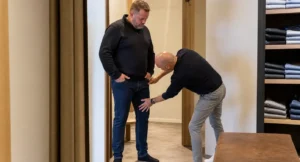Specialist controleert de pasvorm van jeans bij een grote man in een gespecialiseerde kledingwinkel met jeansvakken op de